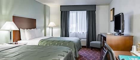 Une chambre d’hôtel avec deux lits, un bureau, une chaise, une télévision et une fenêtre avec des rideaux.