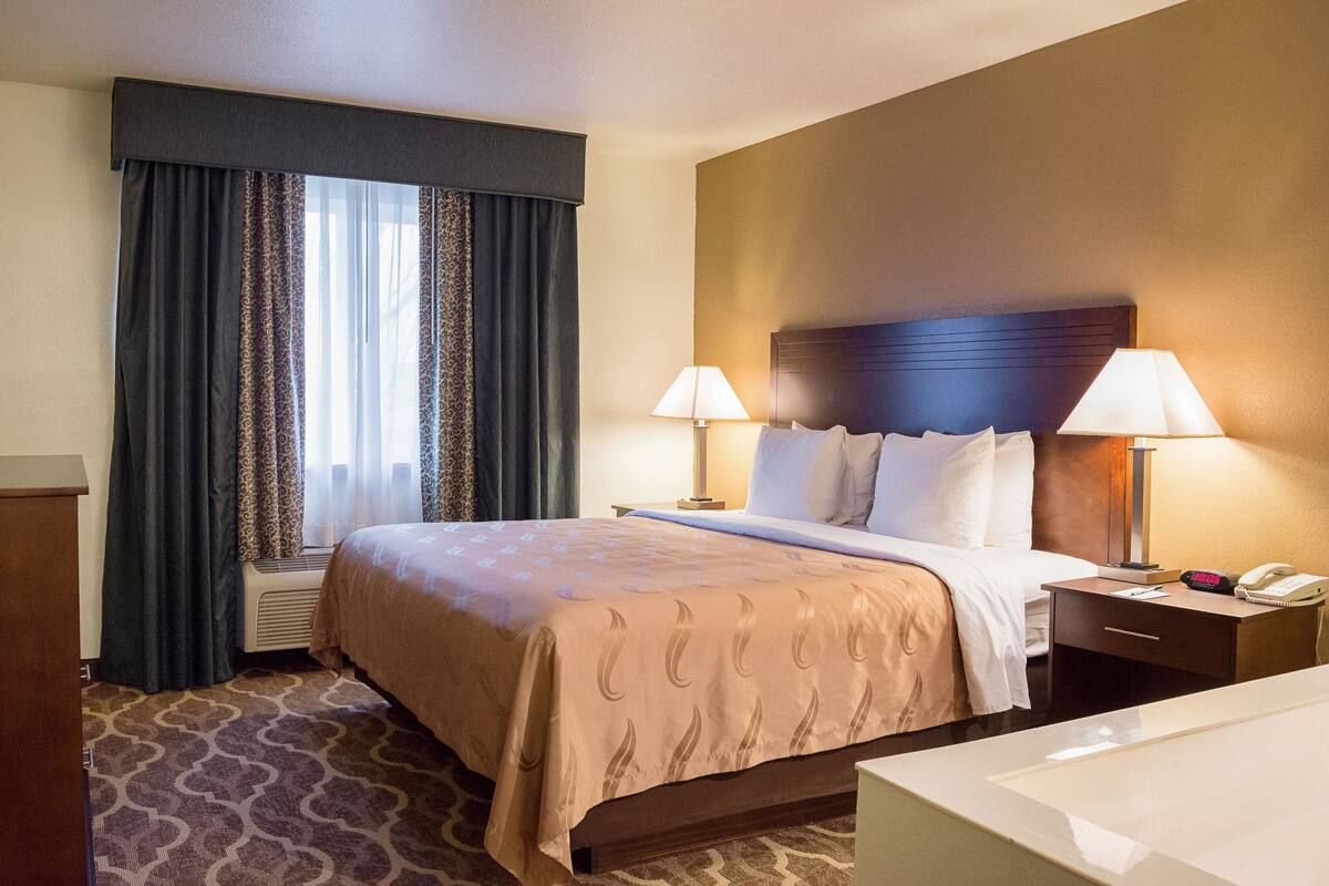 A hotel room with a bed, two bedside lamps, a nightstand, a telephone, and a window with curtains.