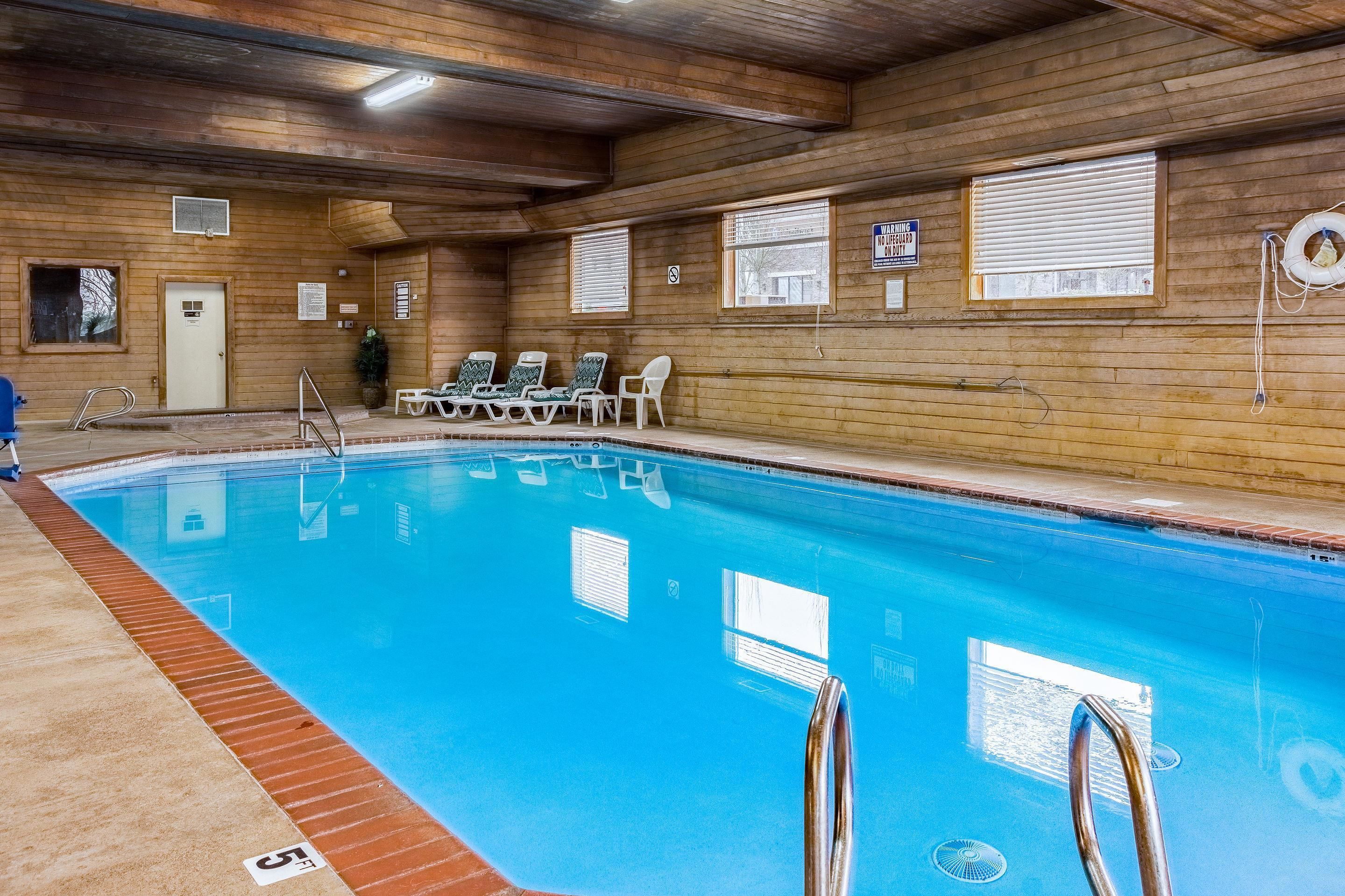 An indoor swimming pool with wooden walls, a clear blue pool, and several lounge chairs.