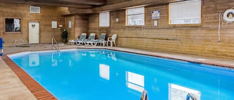 An indoor swimming pool with wooden walls, a clear blue pool, and several lounge chairs.