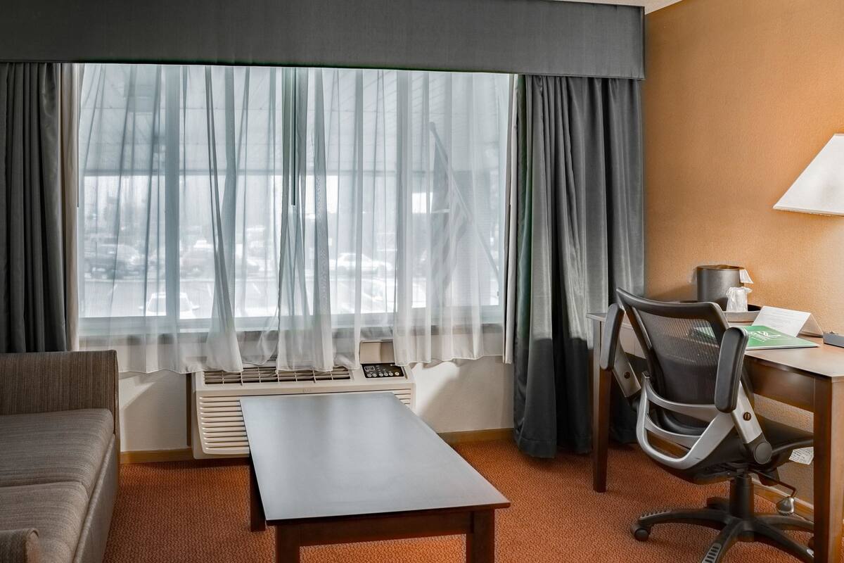 A hotel room with a bed, a desk, a chair, a table, and a window with curtains.