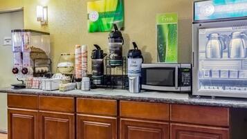 A hotel breakfast area with a coffee station, a microwave, and a refrigerator displaying milk cartons.
