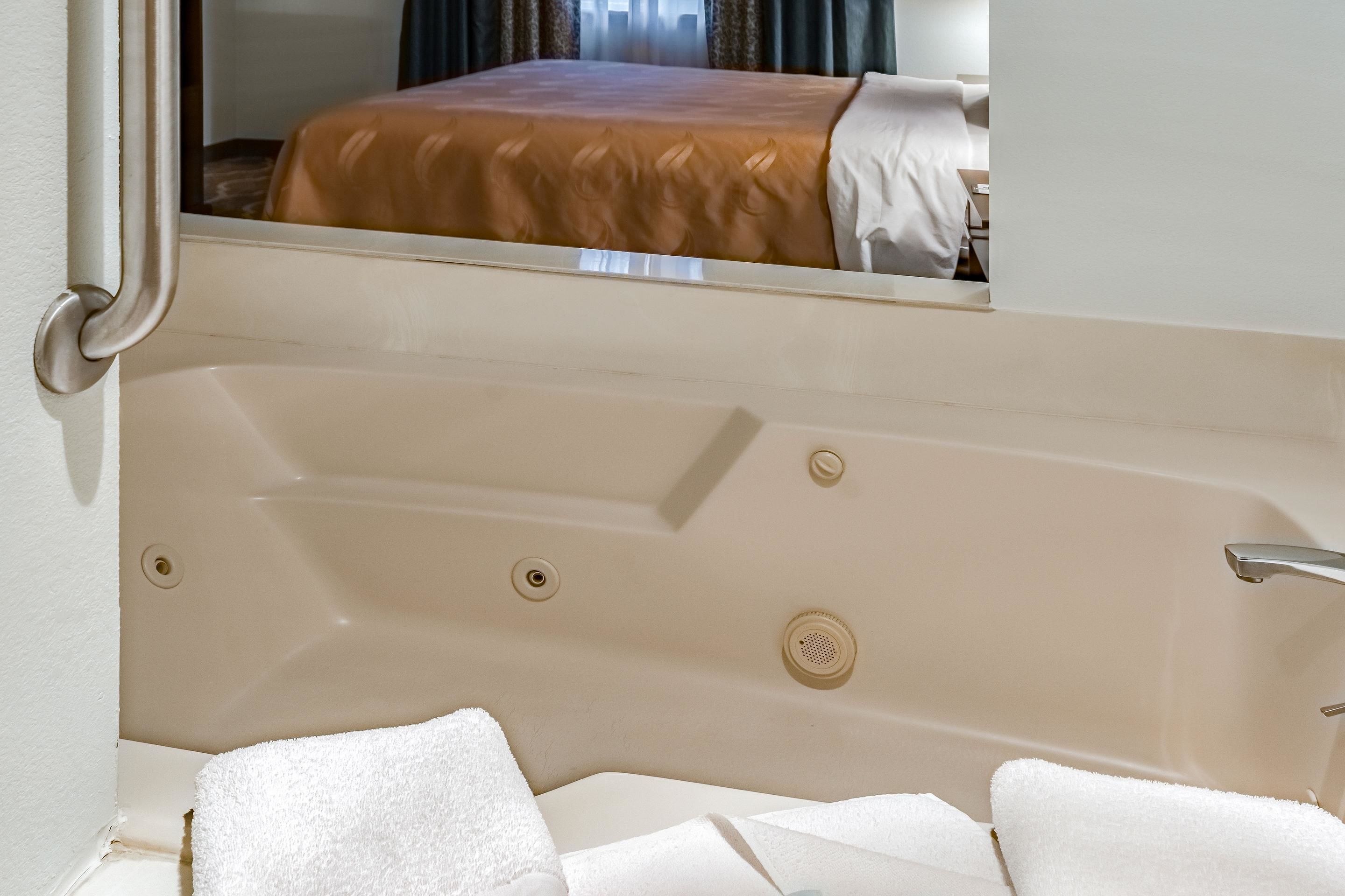 Una bañera con una toalla blanca y, al fondo, una cama con cubrecolcha marrón.