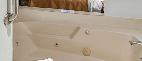 A bathtub with a white towel and a visible bed with a brown cover in the background.