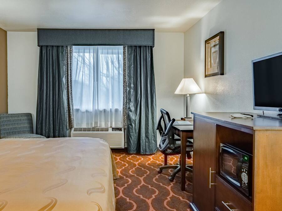 Quarto de hotel com cama, escrivaninha, cadeira, televisão e micro-ondas.