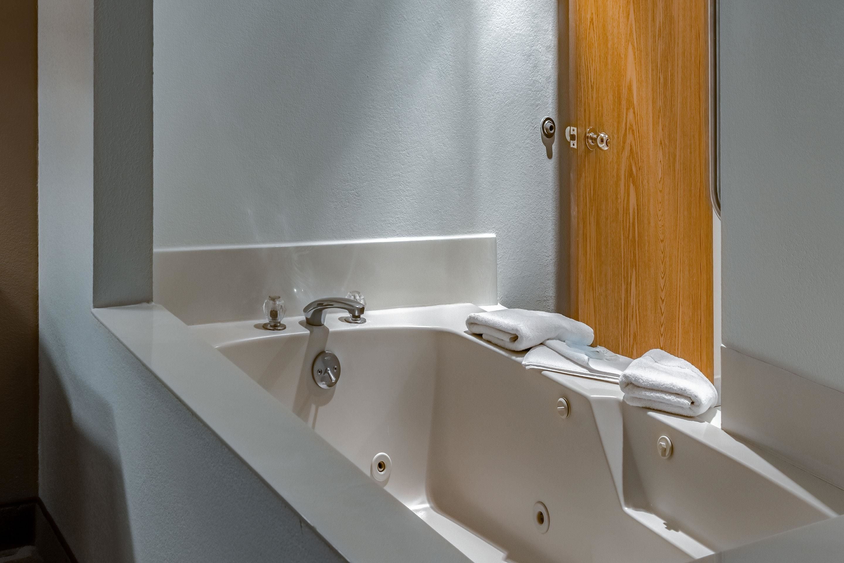 A white bathtub with a wooden door and a towel.
