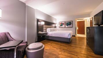 Habitación de hotel con cama, mesita de noche, lámpara, una obra de arte, televisor y un cesto de basura.