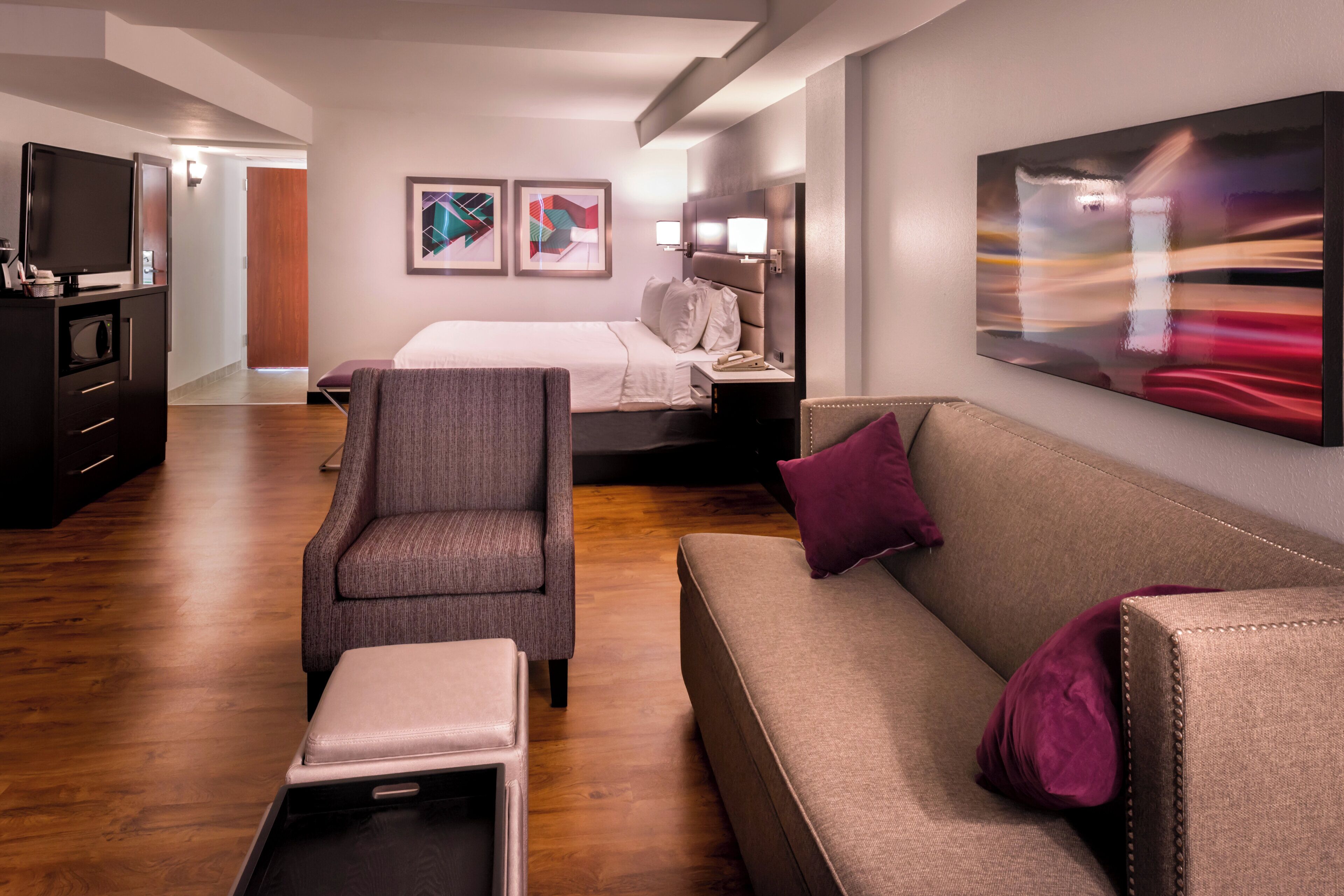 A hotel room with a bed, a sofa, a chair, a desk, and artwork on the walls.