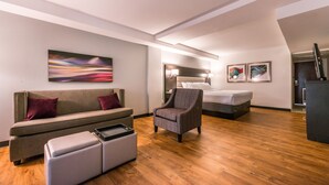 Una habitación de hotel moderna con sofá, sillón, reposapiés y cama.