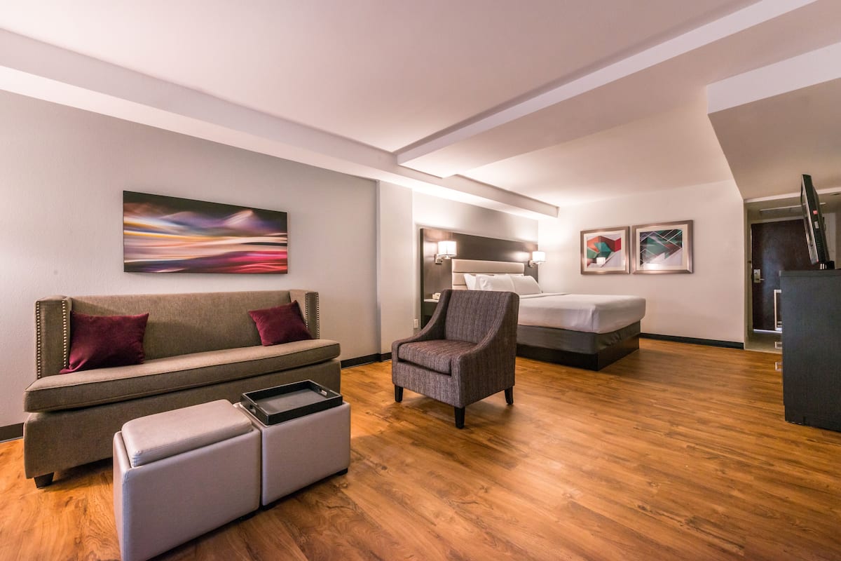 A modern hotel room with a sofa, armchair, ottoman, and a bed.