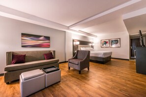 Una habitación de hotel moderna con sofá, sillón, reposapiés y cama.