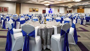 A banquet hall with round tables, chairs with blue sashes, and a stage with a blue backdrop.
