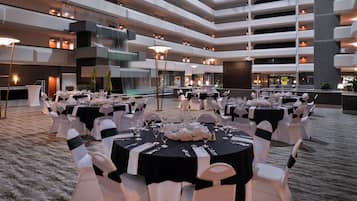 A multi-level indoor event space with round tables set for a formal occasion, featuring a central water feature and modern architecture.