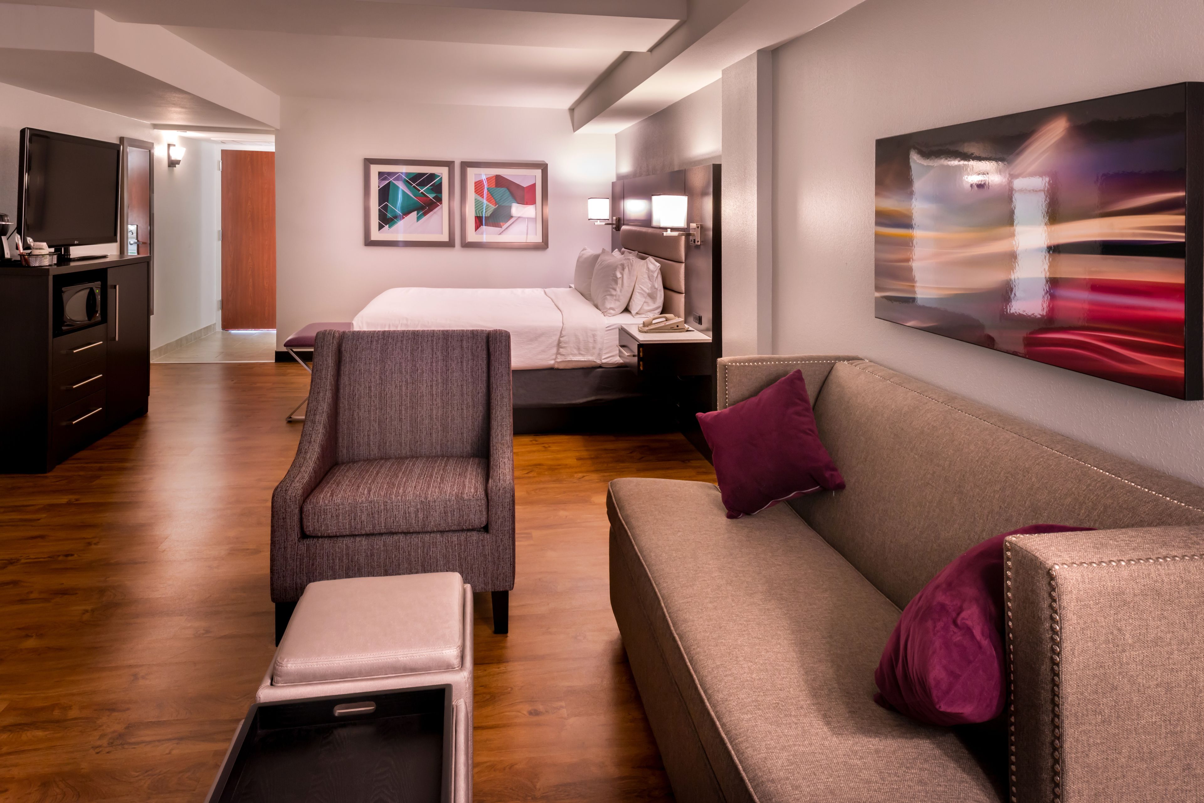 A modern hotel room with a bed, a sofa, a chair, and a desk with a flat-screen TV.