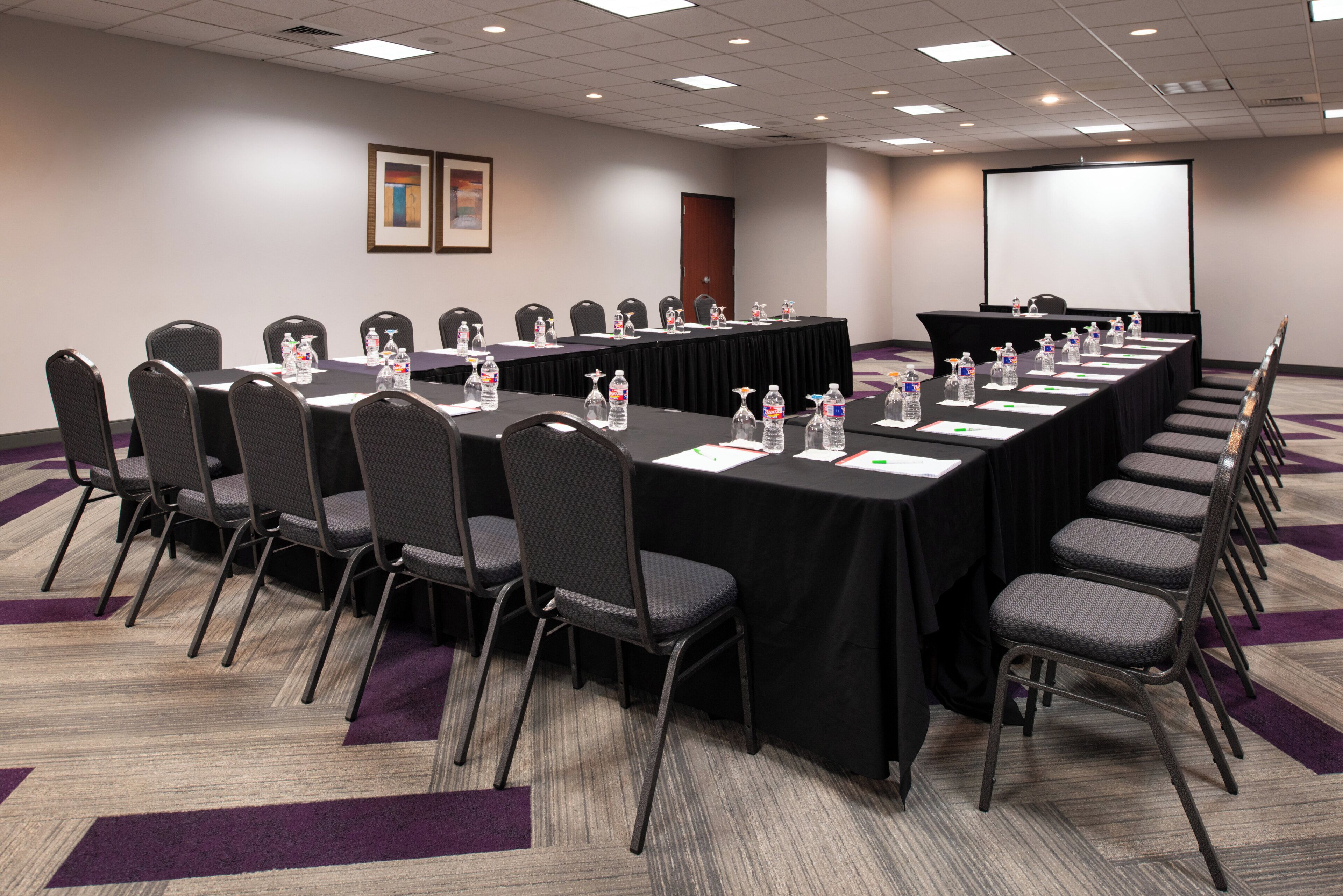 A conference room with a long table, chairs, water bottles, and a projector screen.