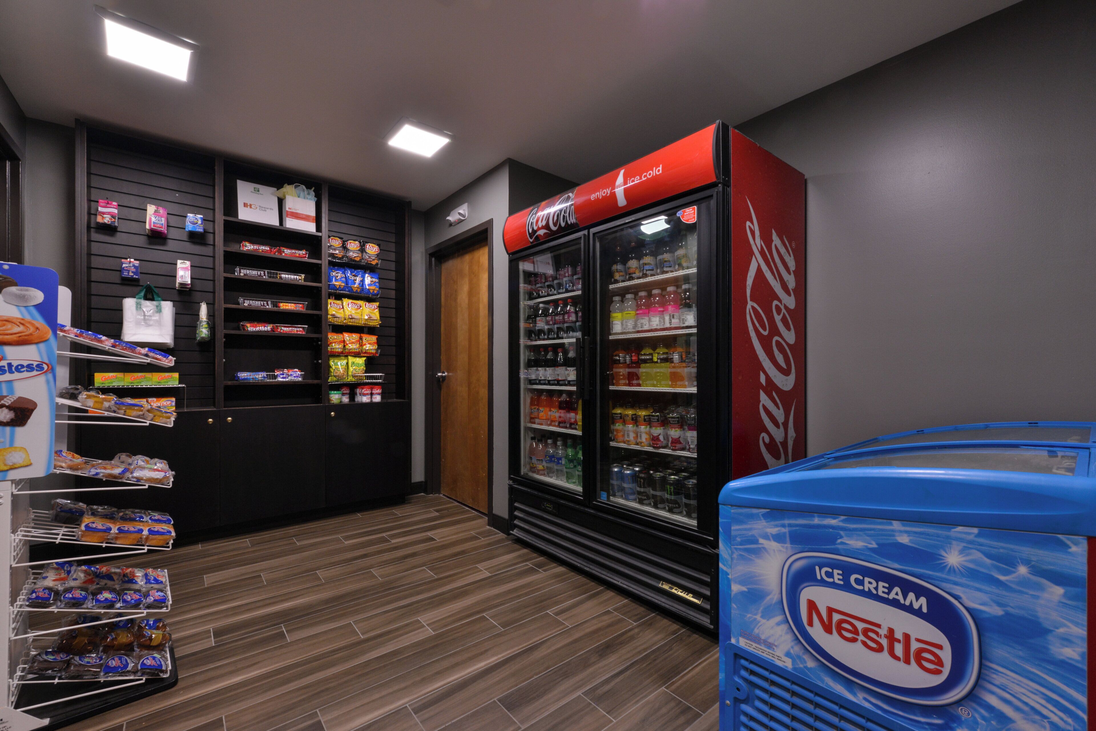Zona de venta automática con varios estantes llenos de aperitivos y un refrigerador con bebidas.