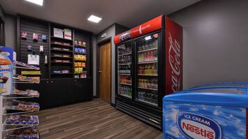 Zona de venta automática con varios estantes llenos de aperitivos y un refrigerador con bebidas.