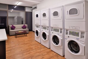 A laundry room with multiple washing machines, a sofa with purple cushions, and a wooden floor.