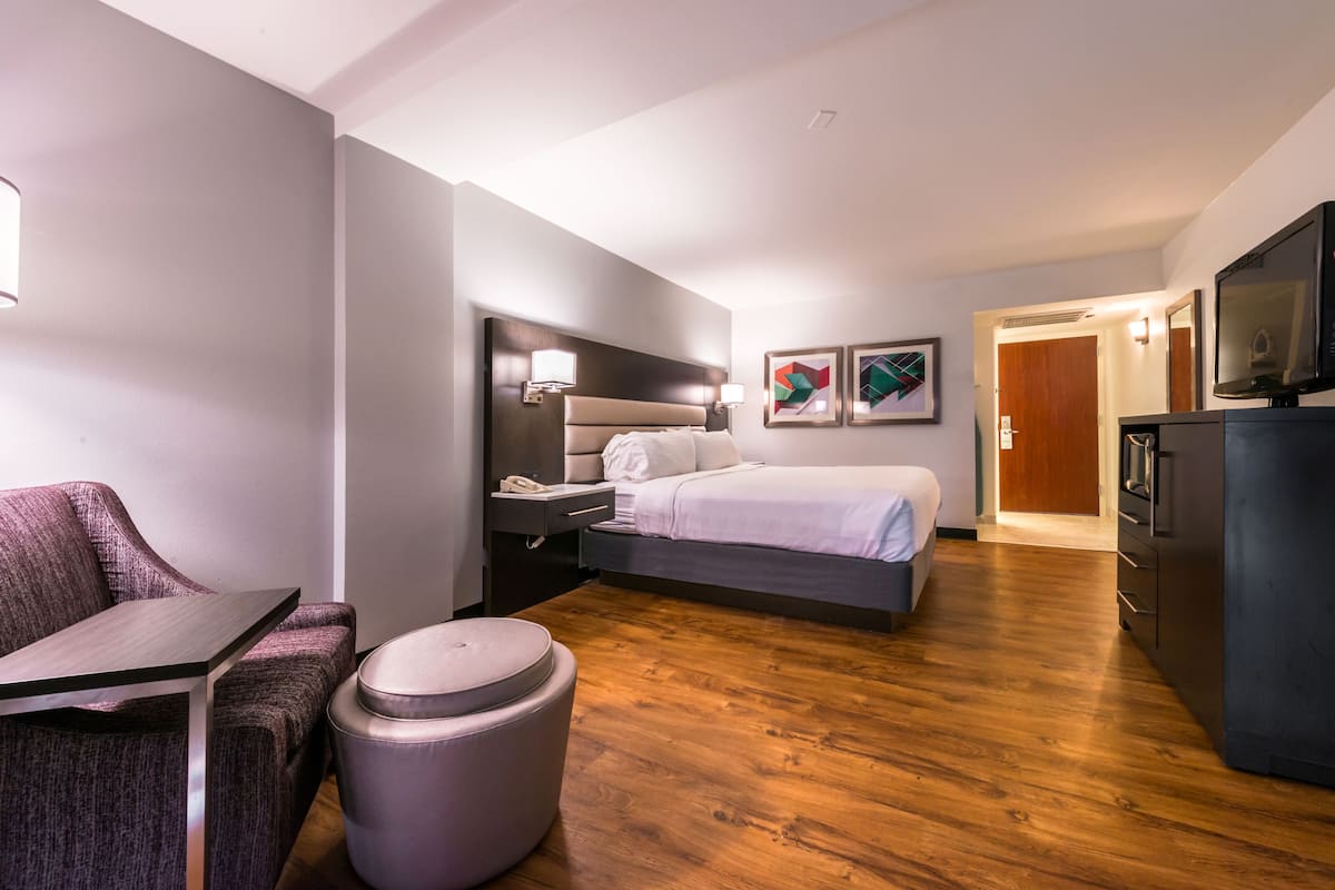 A modern hotel room with a bed, bedside table, lamp, and artwork on the wall.