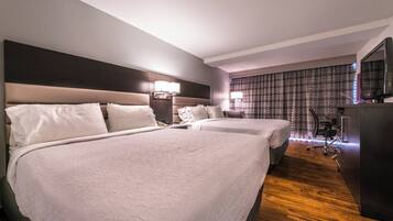 Habitación de hotel con dos camas, un escritorio, un televisor y una ventana con cortinas.