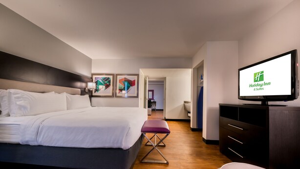 Una habitación de hotel moderna con una cama grande, un televisor mostrando el logotipo de Holiday Inn, piso de madera y una pequeña zona de estar.