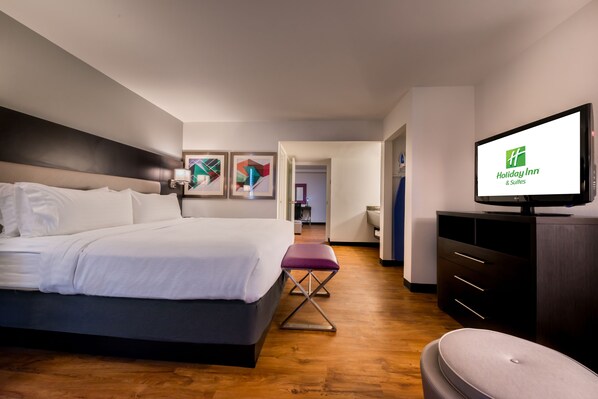 Una habitación de hotel moderna con una cama grande, un televisor mostrando el logotipo de Holiday Inn, piso de madera y una pequeña zona de estar.