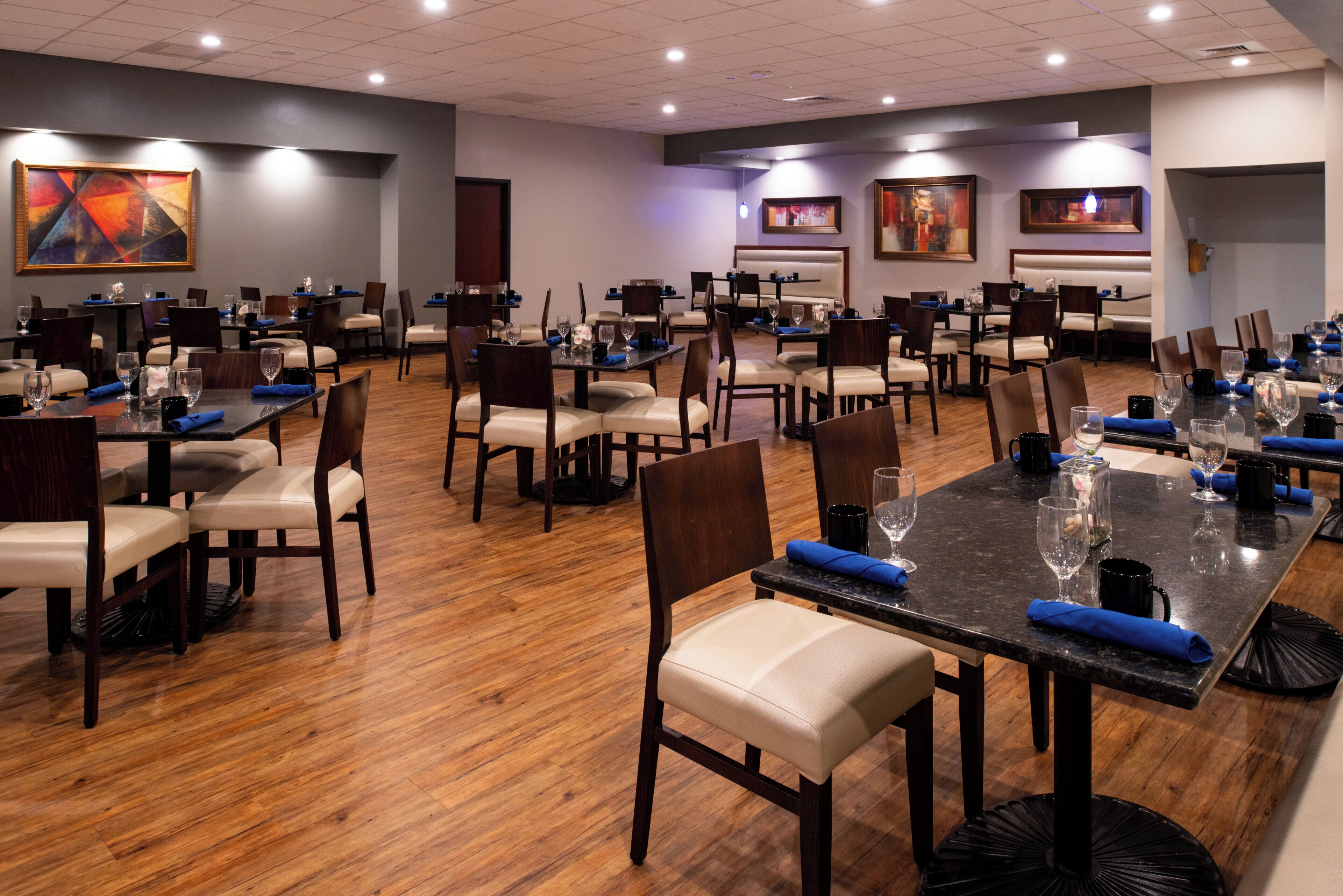 A spacious restaurant with multiple tables and chairs, wooden flooring, and artwork on the walls.