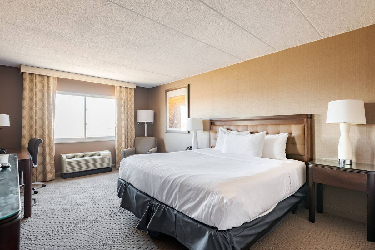 A hotel room with a large bed, a desk, a chair, a lamp, and a window with curtains.