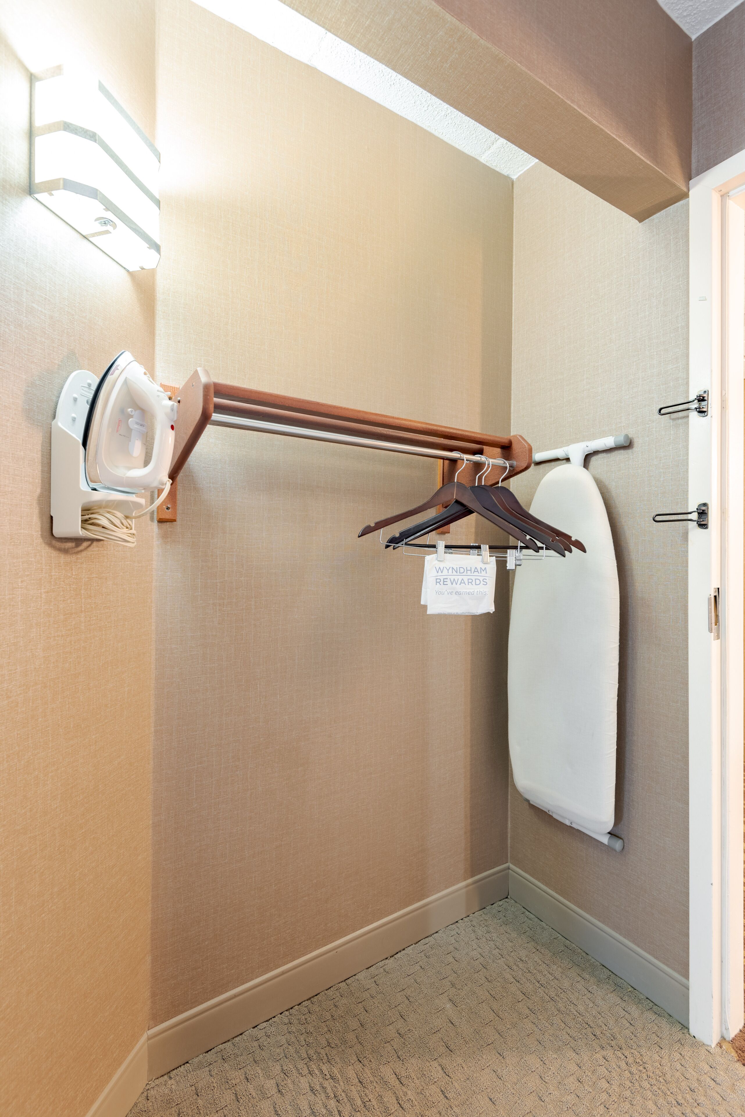 A corner of a hotel room with a wall-mounted ironing board, a hanging towel, and a wall-mounted hairdryer.