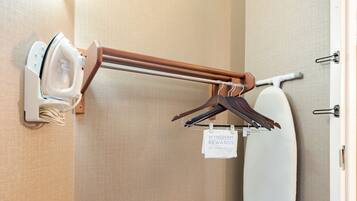 A corner of a hotel room with a wall-mounted ironing board, a hanging towel, and a wall-mounted hairdryer.