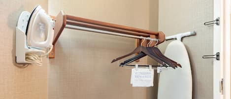 Ein Teil eines Hotelzimmers mit einem Wandbügelbrett, einem aufgehängten Handtuch und einem an der Wand befestigten Fön.