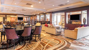 A spacious lobby with a large carpeted area, several seating arrangements, and a television mounted on the wall. - Wyndham Omaha / West Dodge (Omaha)