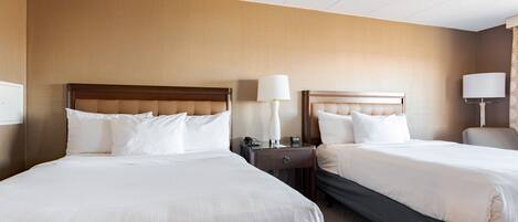Quarto de hotel com duas camas, mesa de cabeceira, luminária e telefone.