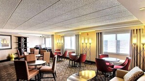 A hotel lobby with a carpeted floor, multiple seating areas with tables and chairs, and large windows providing natural light. - Wyndham Omaha / West Dodge (Omaha)