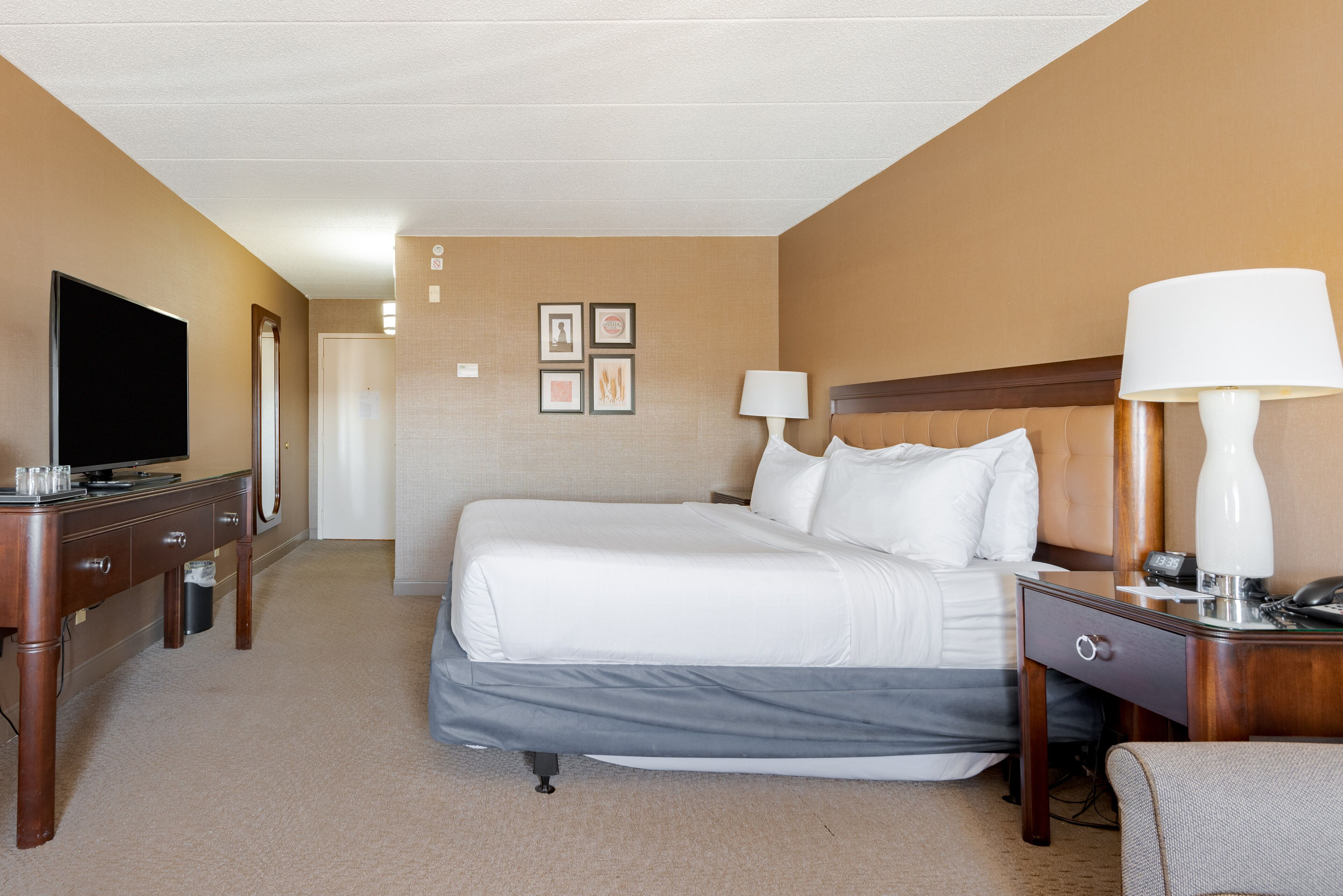 A hotel room with a bed, bedside tables, a TV, and framed pictures on the wall.