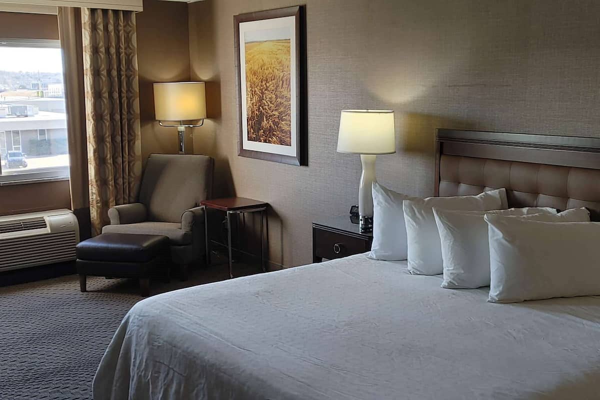 A hotel room with a bed, two bedside lamps, a chair, a small table, and a wall-mounted picture.
