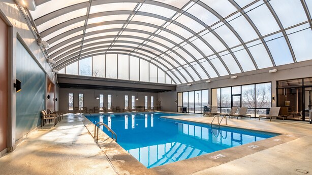 An indoor swimming pool with a glass ceiling, clear windows, and lounge chairs. - Wyndham Omaha / West Dodge (Omaha)