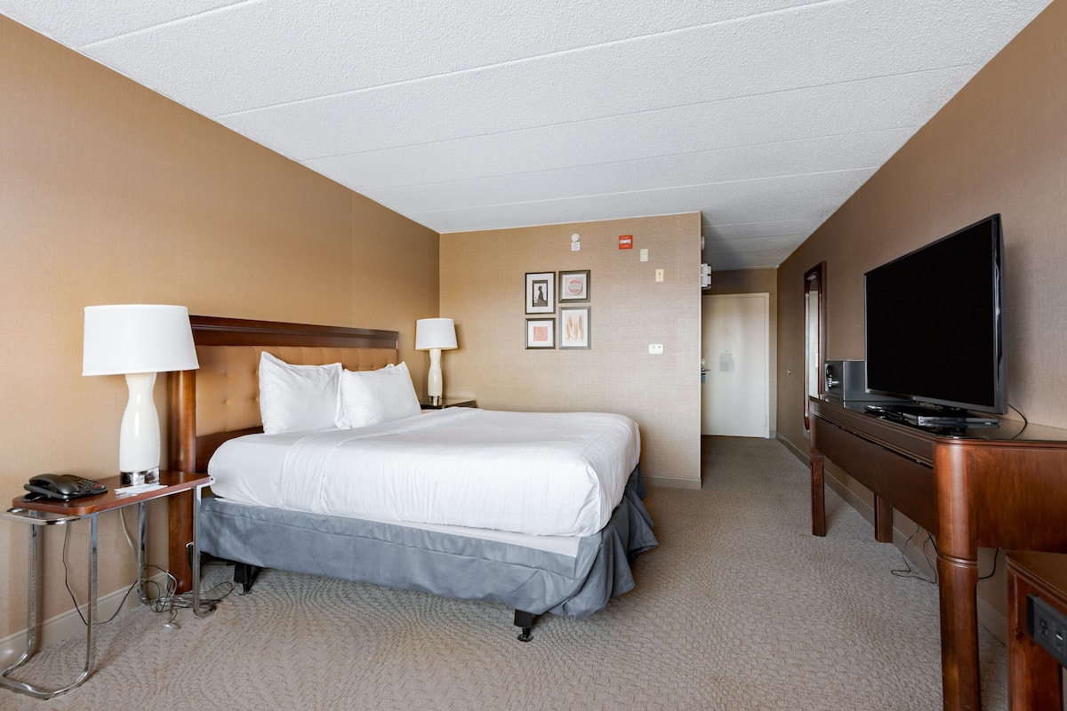 A hotel room with a large bed, two bedside tables with lamps, a flat-screen TV, and a wooden dresser.