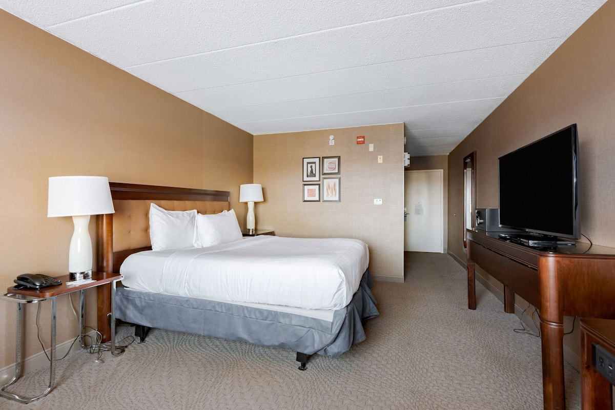 A hotel room with a bed, bedside lamps, a telephone, a television, and a door leading to another room.