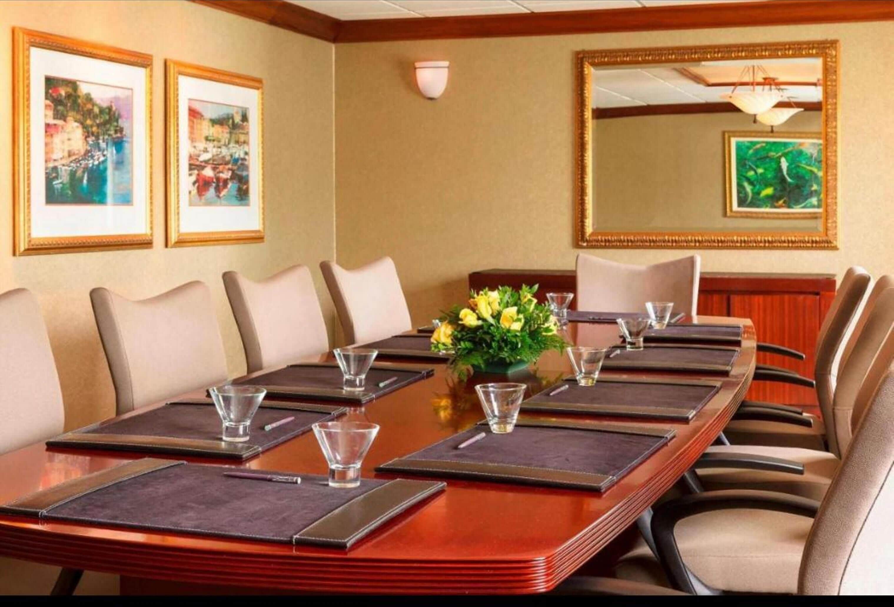 A conference room with a long table, chairs, and framed artwork on the walls.