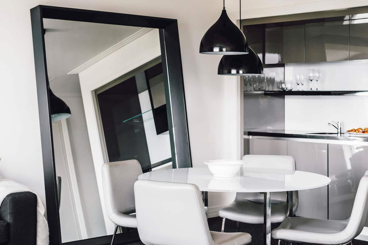 A modern dining area with a round white table and matching chairs, a large mirror, and black pendant lighting.