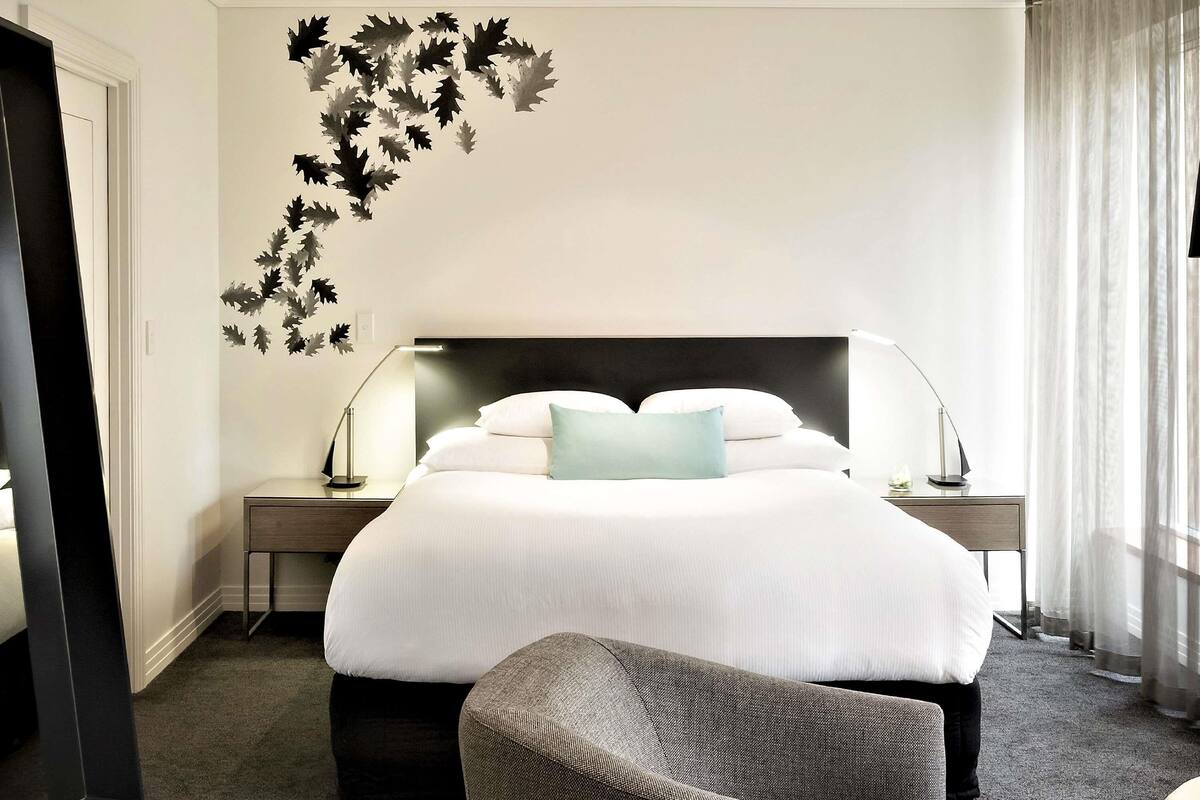 A hotel room with a large bed, two bedside tables, a chair, and a wall decal.
