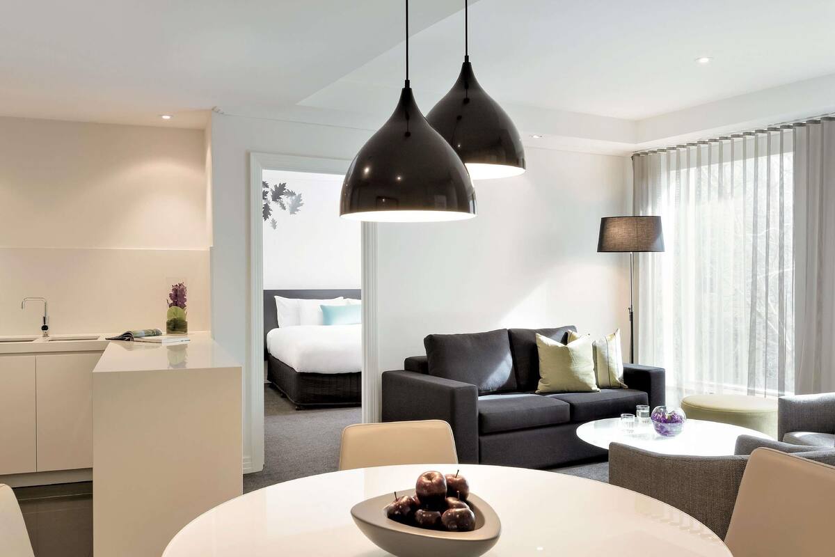 A modern hotel room with a dining area, a sofa, and a bed.