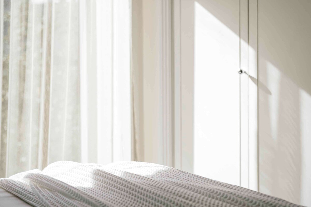 A room with a bed, a window with sheer curtains, and a white wardrobe.
