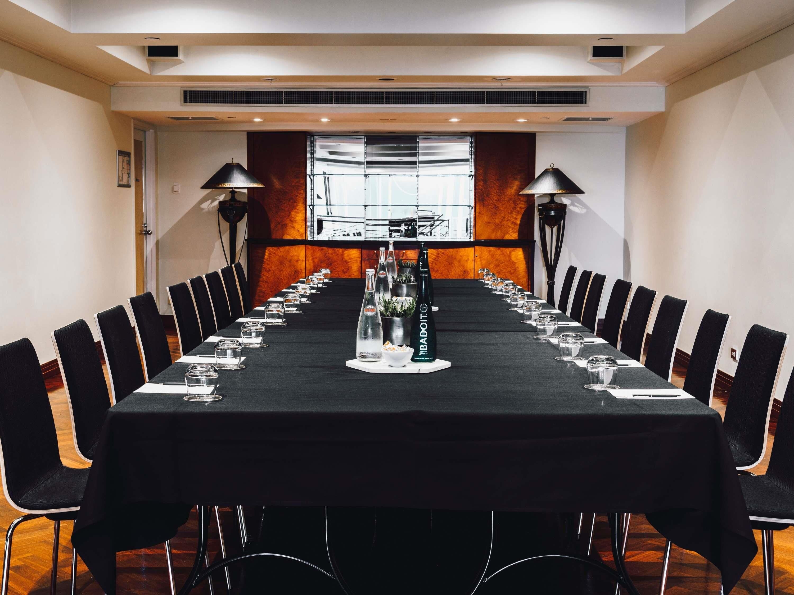 A conference room with a long table, chairs, and two standing lamps.