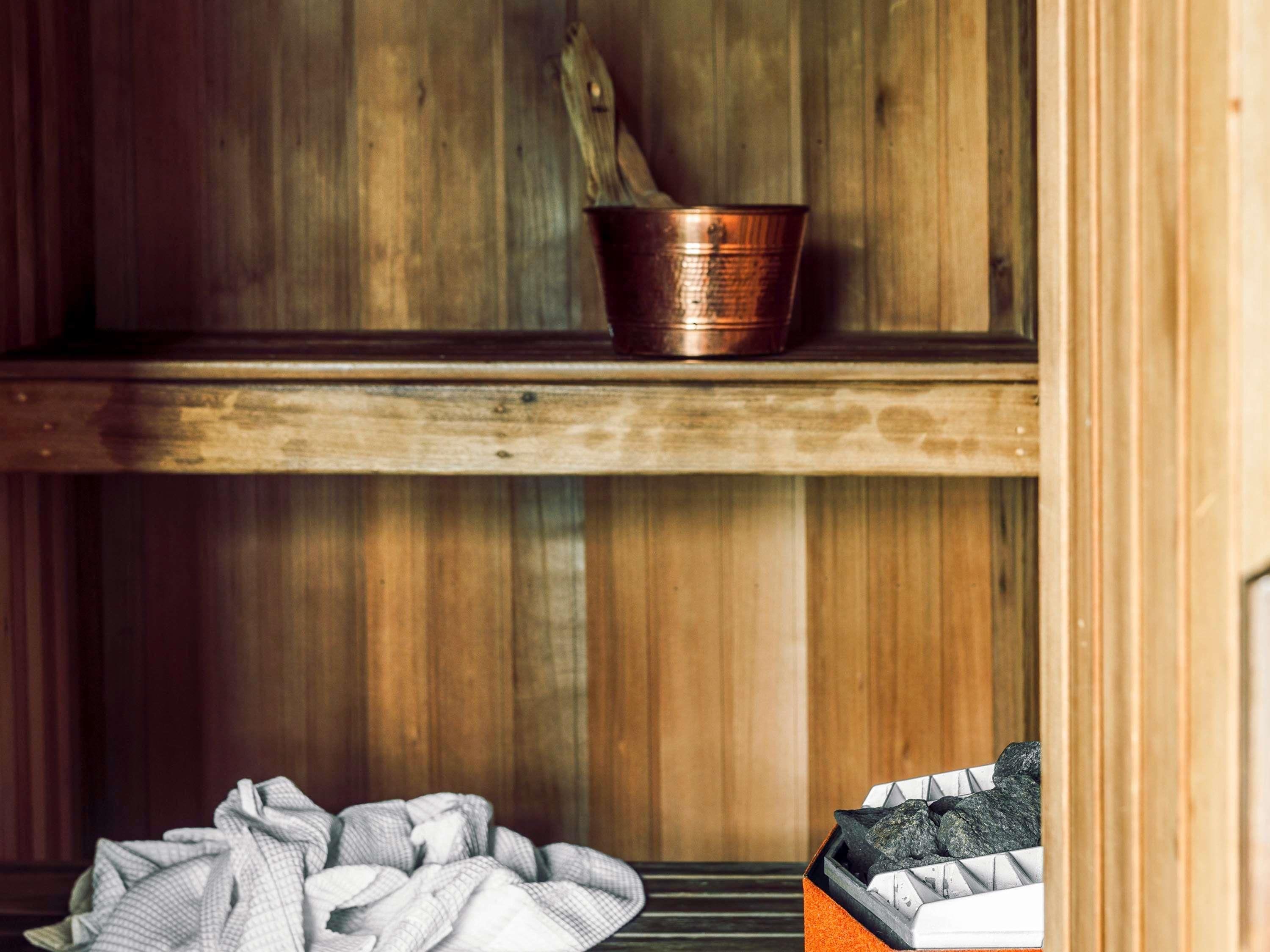 A wooden interior with a copper bucket on a shelf, a pile of blankets on the floor, and a box of charcoal.