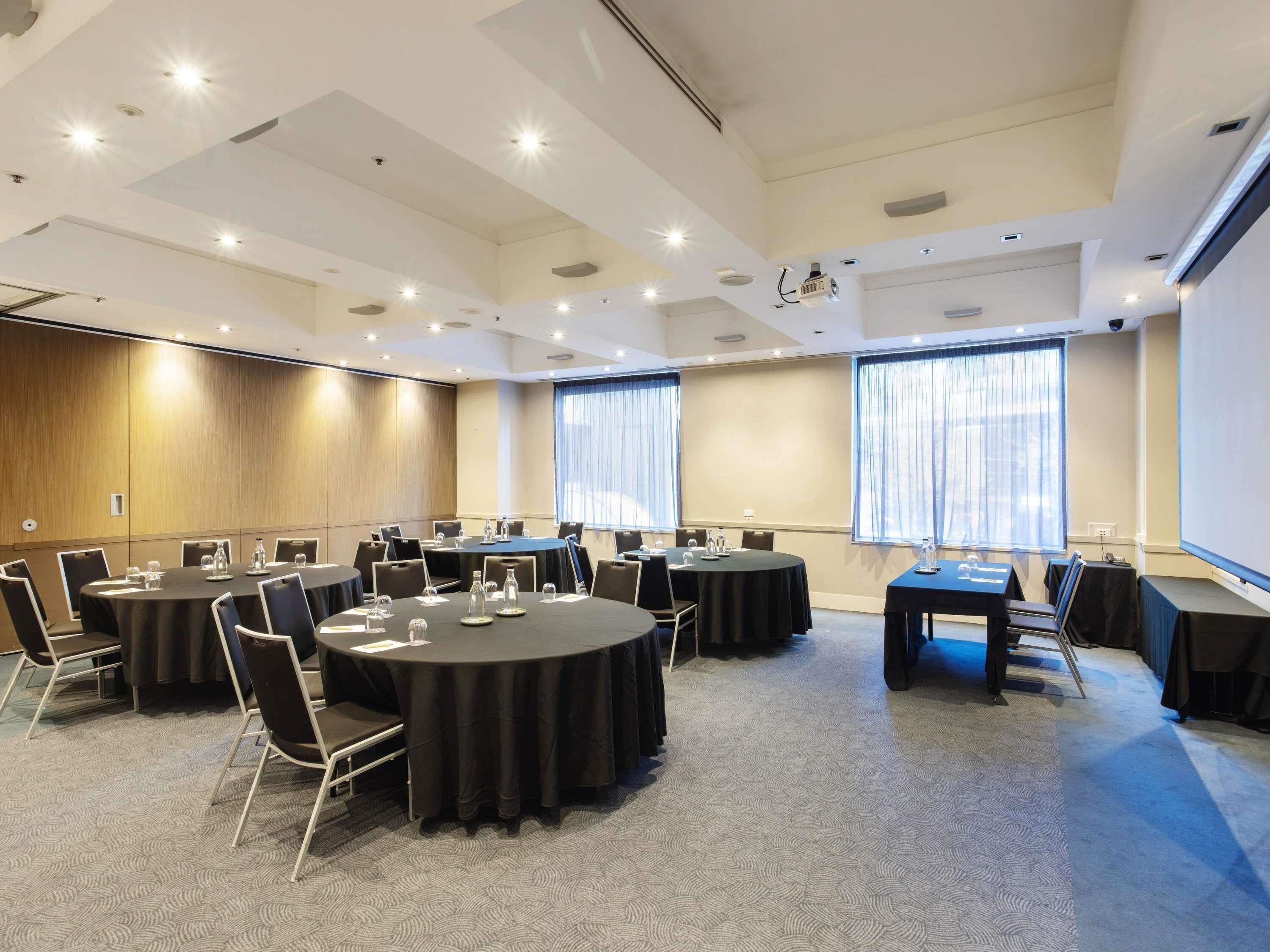 A conference room with round tables, chairs, and a projector screen.