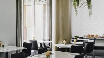 Un comedor moderno con mesas blancas, sillas negras y plantas colgantes.