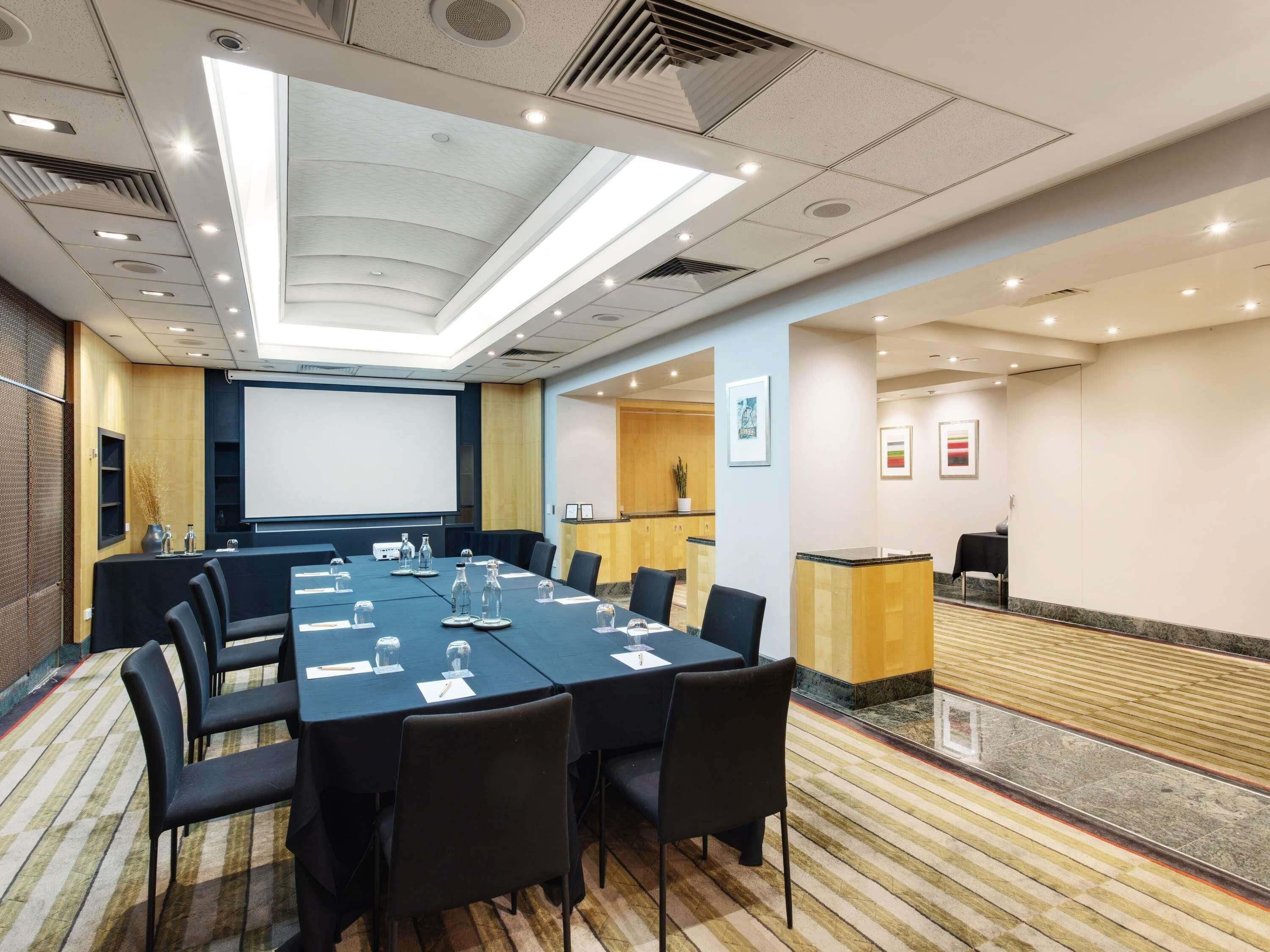 A conference room with a long table, chairs, a projector screen, and a reception desk.