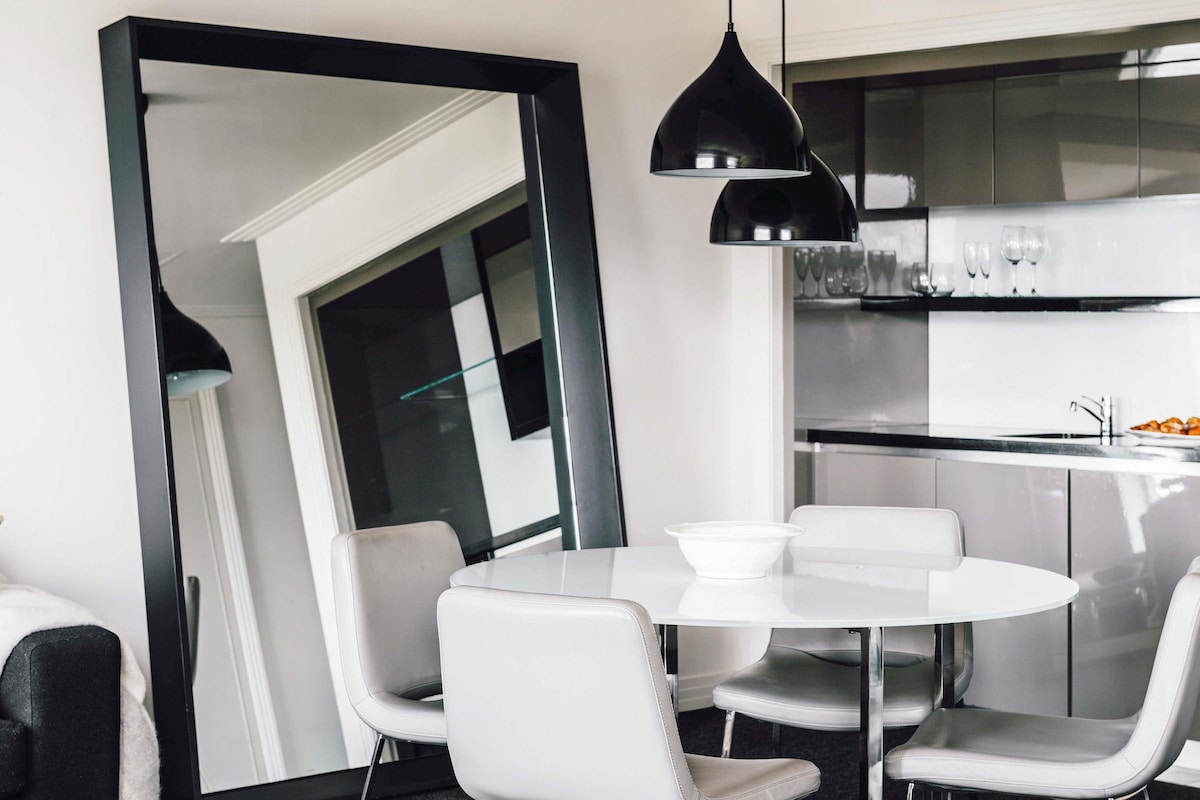 A modern dining area with a round white table and matching chairs, a large mirror, and black pendant lighting.